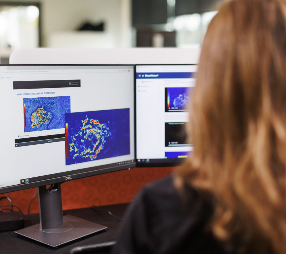 A close-up of a GroundProbe female employee sitting at a desk with multiple computer monitors using the GroundProbe BlastVision software to monitor a mining site