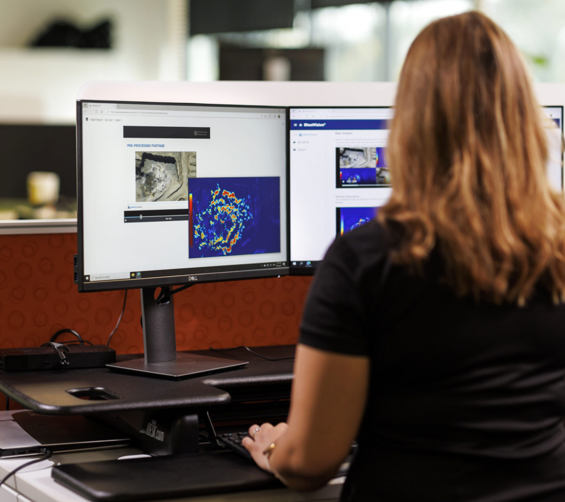 A GroundProbe employee sitting at a desk with multiple computer monitors using the GroundProbe BlastVision software to monitor a mining site