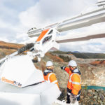 A large Groundprobe white SSR Omni on a mine site in front of two miners wearing orange safety clothes and a white hard hat pointing out at a mine.