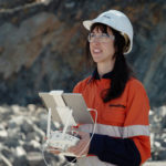 A close-up of a female GroundProbe employee in HPPE gear flying a drone using a tablet and remote controls