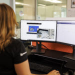 A side view close-up of a GroundProbe female employee sitting at a desk with multiple computer monitors using the GroundProbe BlastVision software to monitor a mining site