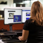 A GroundProbe employee sitting at a desk with multiple computer monitors using the GroundProbe BlastVision software to monitor a mining site